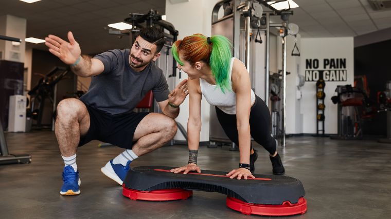 A beginner doing inclined push-ups with a trainer in the gym.