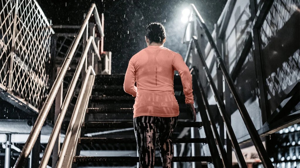 A woman wearing leggings and workout clothes runs up a staircase in the rain at night